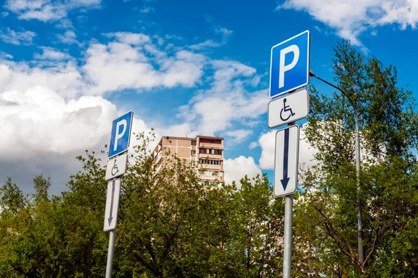 Road sign Parking space for the disabled in a residential area against the background of the sky and green trees. Capital letter P and road sign for the disabled