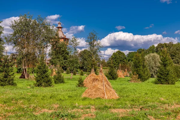 乡村风景 阳光明媚的夏日 一座古老的木制教堂和一堆堆干枯的干草在绿茵的草地上 — 图库照片