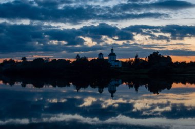 Kilisenin güzel bir yansıması ve sıcak bir yaz akşamında gölün sakin sularında akşam renkli gökyüzü.