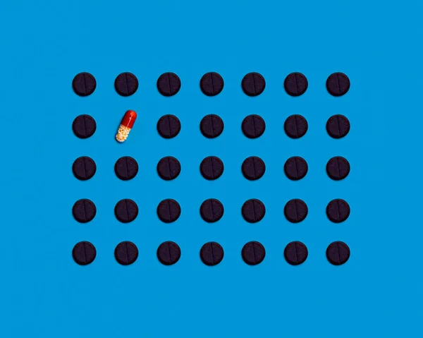 The pattern is made of black pharmaceutical tablets on a blue background. One tablet is a brown-and-white pill. Medical pharmaceutical concept. The concept of loneliness. The concept of vaccine
