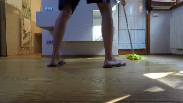 男は着てフリップ フロップ 黄色のモップで寝室の寄せ木細工の床を洗う — ストック動画