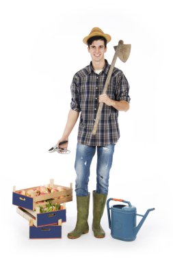 Elini ve çapa ile meyve ve sebze, onun ayak sandıkları, onun omzuna makası ile genç çiftçi bir hasır şapka, ekose desenli gömlek ve yeşil lastik çizme giyiyor