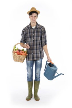 Tek kollu bir sepet meyve ve sebzeler, diğer bir yağmurluk ile tutan genç çiftçi giydiği bir hasır şapka, ekose desenli gömlek ve yeşil lastik çizmeler