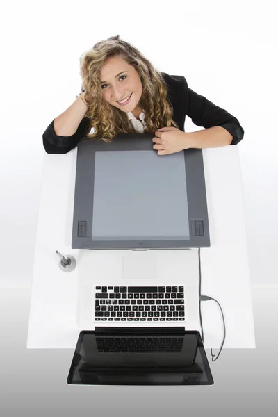 从上面看到的平面设计师拿着平板电脑和笔记本电脑 她面带微笑 双臂放在桌子和头上 — 图库照片