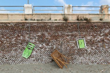 Plaj sandalyeleri ve ahşap masa, bir zincir ve asma kilit, kırmızı tuğla bir duvara asılı kum ve olan mavi bir gökyüzü bulutlu ile korkuluk arasında olduğunu