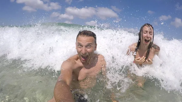 Couple plays amused in the waves at sea