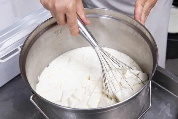Cheesemaker mixes curdled milk with a whisk — Stock Photo, Image