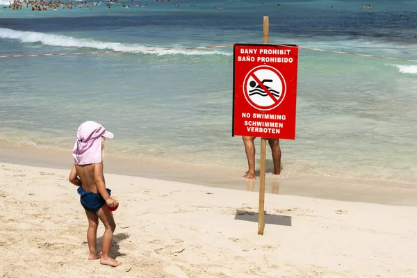 Niño mira un cartel rojo en la playa con una prohibición de baño —  Fotos de Stock