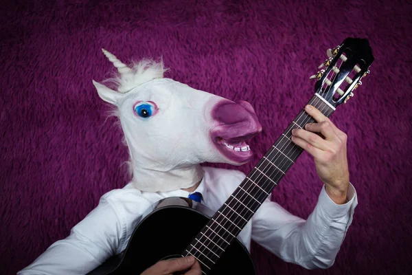 Ausgeflippter junger Mann in lustiger Maske, der auf violettem Hintergrund Gitarre spielt — Stockfoto