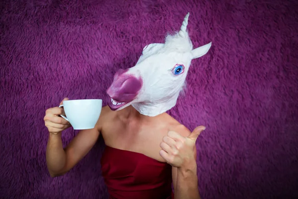 Funny girl unicorn drinks tea and shows thumbs up gesture