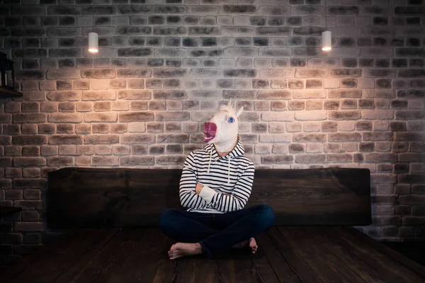 Insolito giovane uomo in maschera comica si siede da solo sul letto — Foto Stock