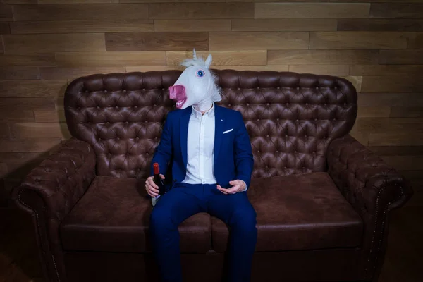 Rolig unicorn i elegant kostym sitter på soffan med en flaska vin — Stockfoto