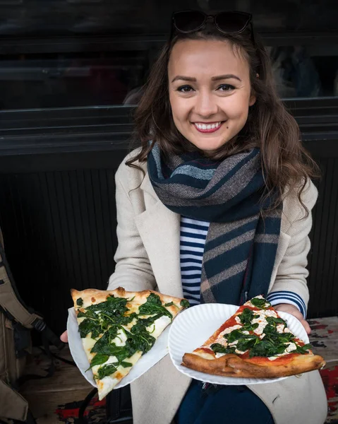 Šťastná mladá žena má dvě velké kousky pizzy Stock Obrázky