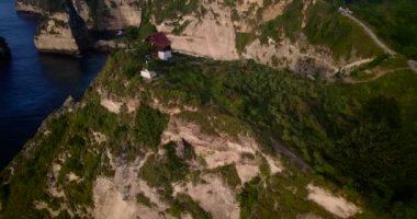Kırmızı elbiseli genç kadın koy ve kayalar okyanus dalgalarıarka planda ev up. Sahilde ve dağlarda uçan drone görünümü. Bali, Endonezya