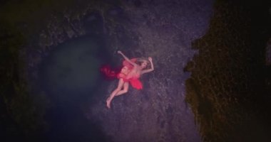 Pembe elbiseli genç kadın, taş ve kayaların yanında doğal havuzda tek başına yatıyor. Uçan ve dönen drone görünümü. Bali, Nusa Penida, Endonezya