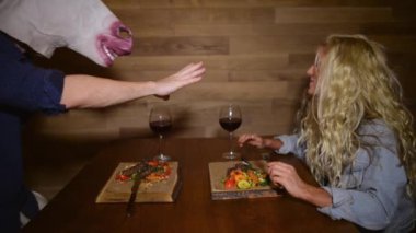 Komik bir tek boynuzlu at maskesi adam kız arkadaşı karşısında yiyecek ve şarap ile masada oturur. Sıradışı bir erkekle birlikte akşam yemeği yiyen genç bir kadın. Garip çift.