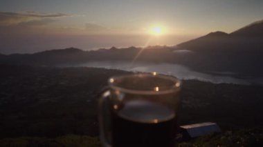 Adam el dağların arka planda kahve ve gündoğumu ile cam tutar. Sabahın erken saatlerinde göldeki volkanın tepesinden güzel manzara. Bali, Endonezya