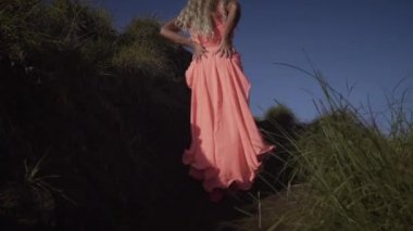 Pembe elbiseli yalınayak genç kadın üzerinde geri görünümü yürüyüş ve gökyüzü arka planda volkanın üstüne siyah iz üzerinde yükselen.