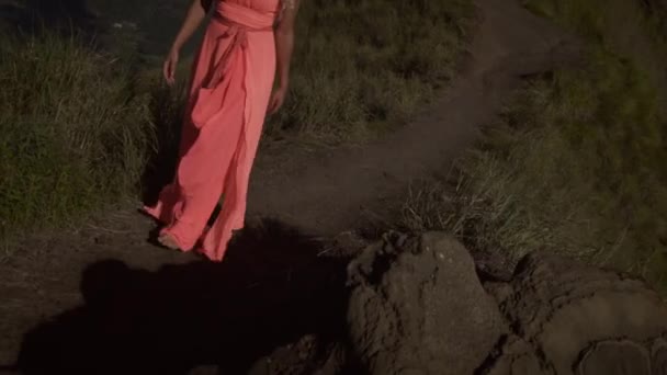 前视图赤脚的年轻女子在粉红色的礼服走在黑色的沙小径上 在绿草和山脉的背景上升在火山顶部 — 图库视频影像