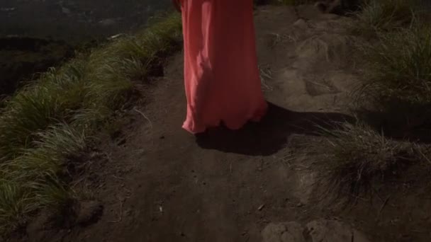 身着粉红色连衣裙的赤脚年轻女子在山 湖泊和天空的背景下 走上黑色的沙路 前往火山边缘 女孩看惊人的景色 — 图库视频影像