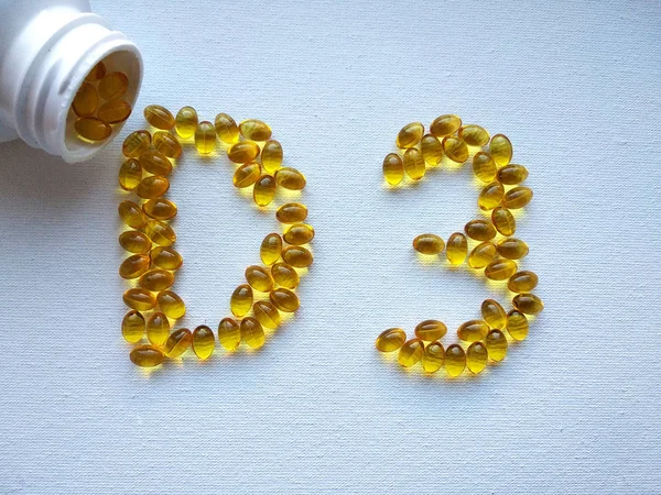 D vitamini içeren sarı yağ kapsülleri plastik şişeden dökülür ve beyaz arka planda D3 şeklini oluşturur