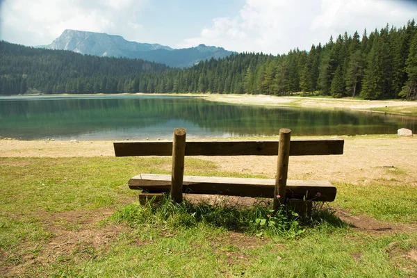在山景秀丽的湖畔没有人的长椅。 阳光灿烂的日子。 黑山的性质。 黑湖. 免版税图库照片