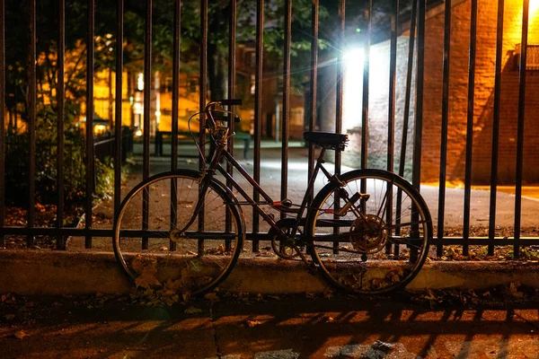 A bike locked to a park fense at night