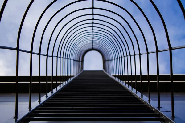 A metal rounded staircase on the wall of the building. Reduced perspective, blue sky