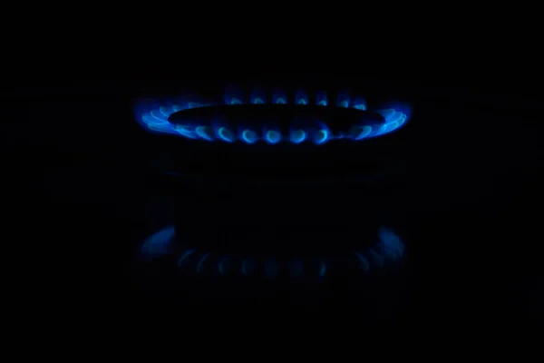 Circles of fire on a gas stove in the dark. Blue flame reflected on the surface