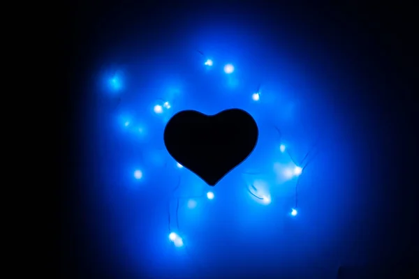Black heart in the dark surrounded by blue garlands. Flaming heart. Valentine\'s day and Valentine\'s day on February 14.