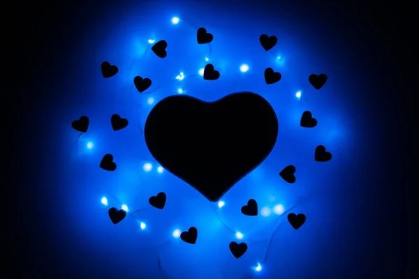 Black heart in the dark surrounded by small hearts and blue garlands. Flaming heart. Valentine\'s day and Valentine\'s day on February 14.