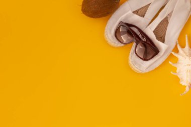 Yaz tatili ve plaj tatili. Güneş gözlüğü, beyaz espadrille, hindistan cevizi, sarı arka planda deniz yıldızı. Seyahat ya da tatil kavramı.