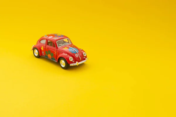 Gorodok, Belarus - 15 July 2020 : Red toy car with painted colorful flowers on a yellow background. Minimalism. Women\'s Gift Concept