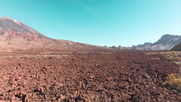 Sparatoria aerea con droni. Deserto paesaggio vulcanico in rosso. Pietre e una montagna con un vulcano contro il cielo blu. Il concetto di colonizzazione e voli verso Marte e altri pianeti — Video Stock