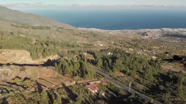 Un disparo aéreo. Vuelo sobre una nueva carretera de montaña de asfalto en la que los coches se mueven. Nuevas marcas de tráfico. giro de horquilla. Rodeado de bosques marinos de pinos verdes, nubes bajas, cielo azul y cordillera — Vídeo de stock