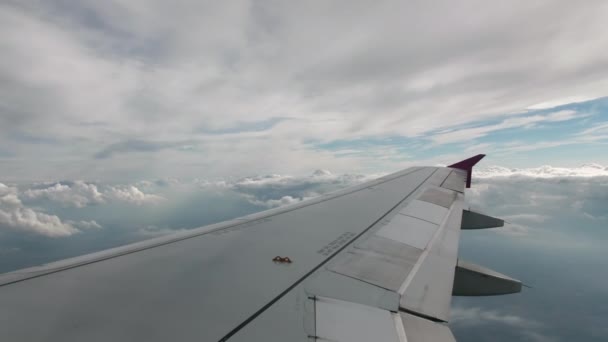 Vuelo del avión a nivel de vuelo, sobre el fondo del cielo azul y las nubes volumétricas texturales. Vista desde la cabina, en primer plano un ala gris de un avión con alas rosadas — Vídeos de Stock