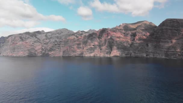 Antenn skott. En enorm svart-röd vulkanisk bergart är ett berg i det blå vattnen i havet. Mot den blå himlen. Kanarieöarna, Teneriffa — Stockvideo