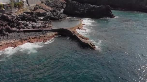 Aerial Shot. Circular flight on a sunny day over the coast of the ocean and the rocky volcanic coast about which blue waves are beating. Tourists and vacationers swimming in the natural pool with — Stock Video
