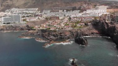 Hava atış. Dağ tatil beldesi birçok otel, palmiye ağaçları ve diğer bitki örtüsü. Mavi okyanus ve volkanik sahilde yenerek dalgalar. Hangi kimliği belirsiz turist yüzmek doğal havuzda. Büyük bir