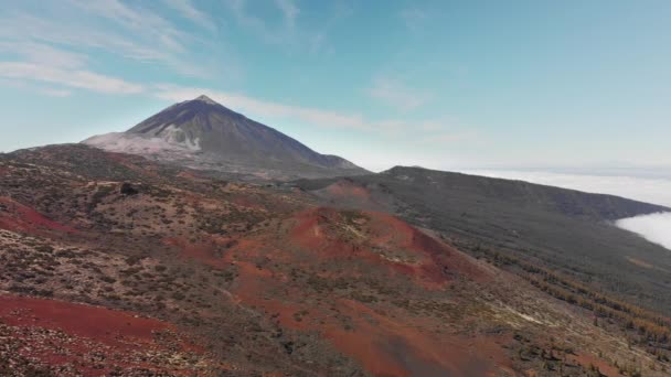 Aerial shot. Flying above the clouds on the background of the peak of the volcano and alpine forest of pine needles and red volcanic landscape. Mountain range from a height. Canary Islands, Teide — Stock Video