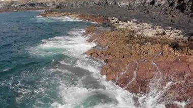 Hava atış. Dairesel operasyonlarla volkanik kıyı. Manzara sarı ve kahverengi renk ve onlar hakkında okyanus sahilde yenerek dalgalar büyük taşlar var. Yakın çekim