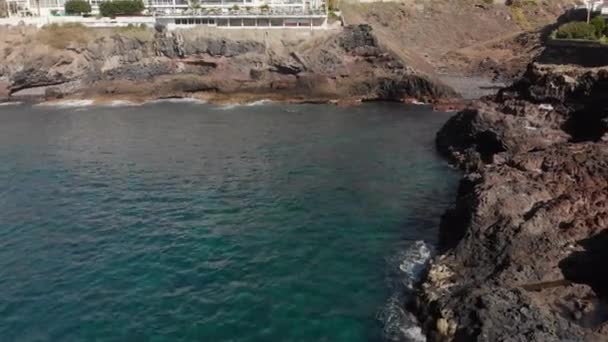 Luftfoto. Flyv tilbage langs den vulkanske kyst. Landskabet er store sten af gul og brun farve og slå om dem turkise bølger på stranden af havet. I baggrunden er hoteller – Stock-video