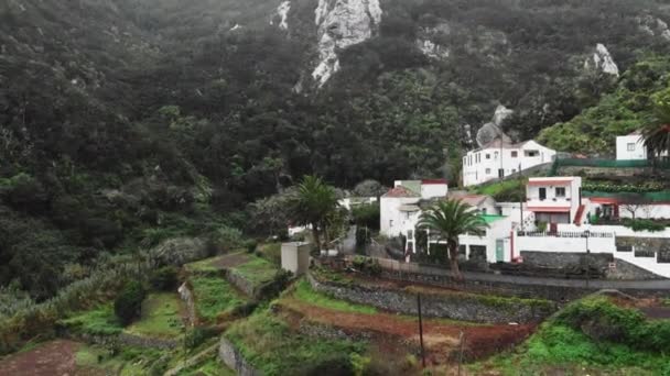 Un disparo aéreo. Pueblo de las tierras altas en un cañón entre dos colinas y montañas. Nubes de tormenta baja. Palmeras y densa vegetación tropical. El concepto de trabajo en casa y freelance. Tenerife, Canarias — Vídeo de stock