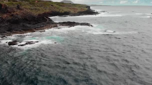 Stormachtige Oceaan, witte schuim uit de golven die treffer de kustlijn van bevroren vulkanische lava. In de achtergrond zijn bergen en de blauwe hemel. Luchtfoto schot. Garachico, Tenerife, Canarischeeilanden — Stockvideo