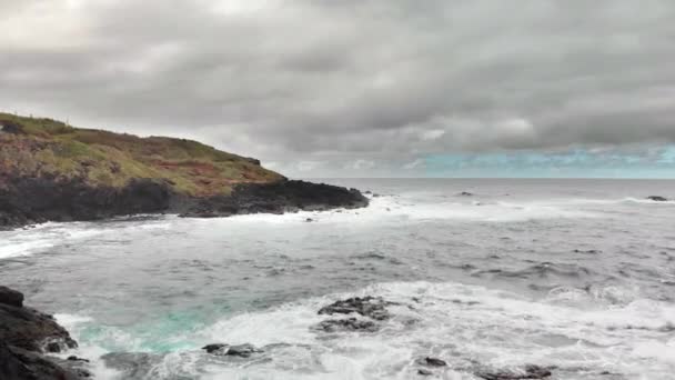 狂风暴雨的海洋, 来自海浪的白色泡沫, 冰封的火山熔岩的暗礁。背景是山和蓝天。楼梯下到海里。空中射击。Garachico, Tenerife — 图库视频影像