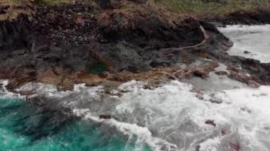 Panorama dikey, dik volkanik shore, fırtınalı okyanus, beyaz köpük kıyı şeridi vuran dalgalardan. Arka planda dağlar ve mavi gökyüzü vardır. Merdiven denize. Hava atış. Garachico