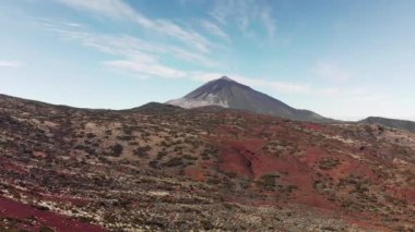 Hava atış. Açık güneşli bir volkanik dağ vadisinde Teide yanardağı üst zirvesine. Ön planda bir kırmızı volkanik toprak ve sıradışı zanaat bitki örtüsü, uçuşlar kavramı var.
