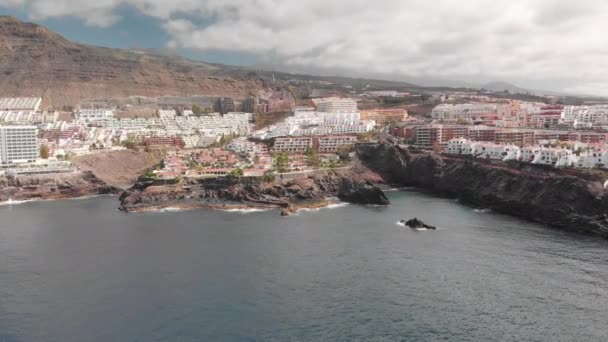 Aerial Shot. Mountain resort town with many hotels, palm trees and other vegetation. Blue ocean and the waves beating on the volcanic shore. huge stone in the foreground. Peak the top of the volcano — Stock Video