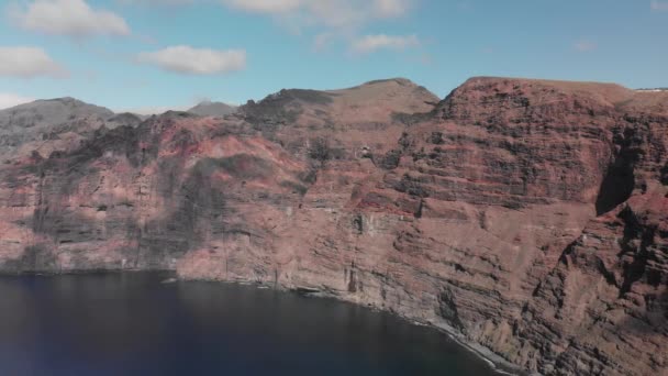 Luftaufnahme. Ein riesiges schwarz-rotes Vulkangestein ist ein Berg im blauen Wasser des Ozeans. gegen den blauen Himmel. Kanarische Inseln, Teneriffa, los gigantos — Stockvideo