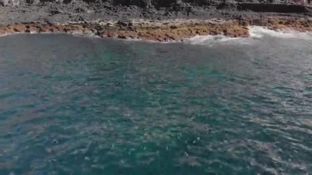 Tiro aéreo. Oceano azul e turquesa com ondas espumantes. A costa vulcânica é a superfície textural de uma praia de montanha. Dolly tiro close-up — Vídeo de Stock